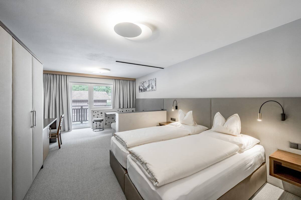 A modern hotel room with two beds, a desk, and a chair.
