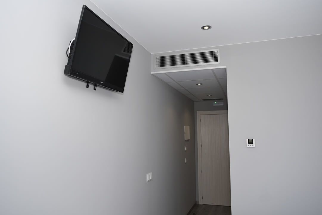Un passadís amb una televisió penjada, una porta i un interruptor de llum.