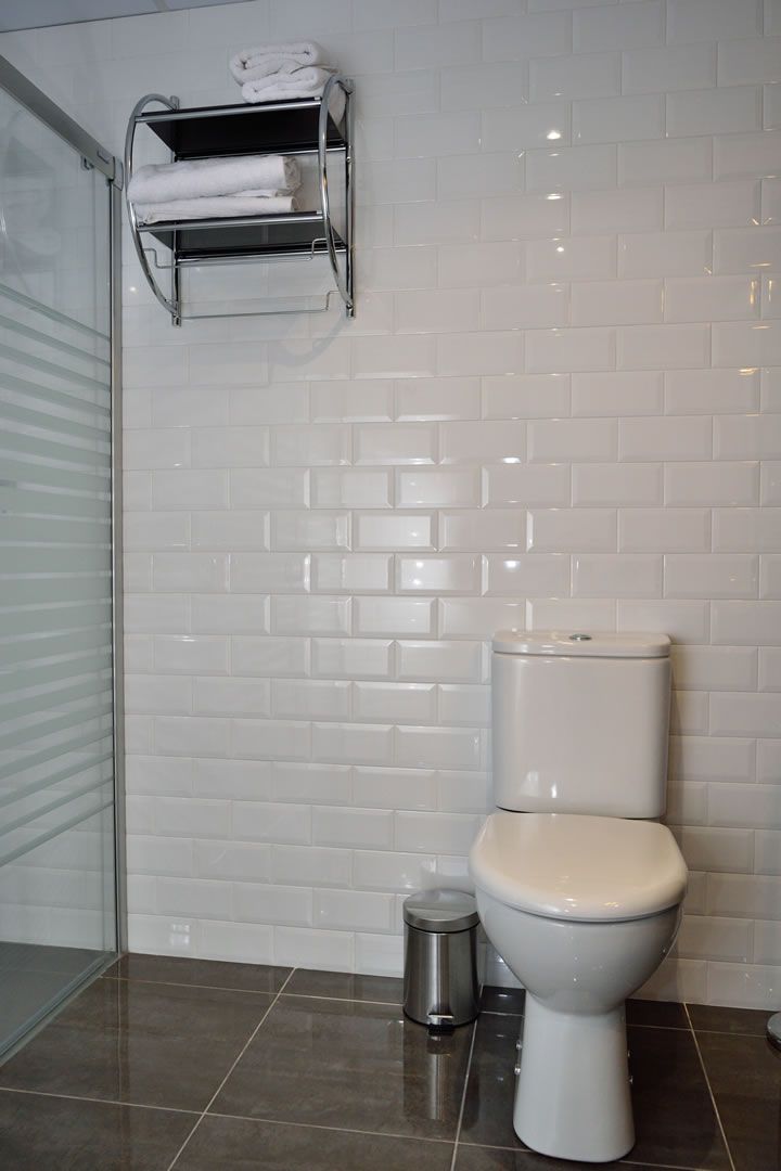 A bathroom with a toilet, a trash bin, and a towel rack with folded towels.