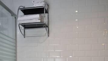 A bathroom with a toilet, a trash bin, and a towel rack with folded towels.