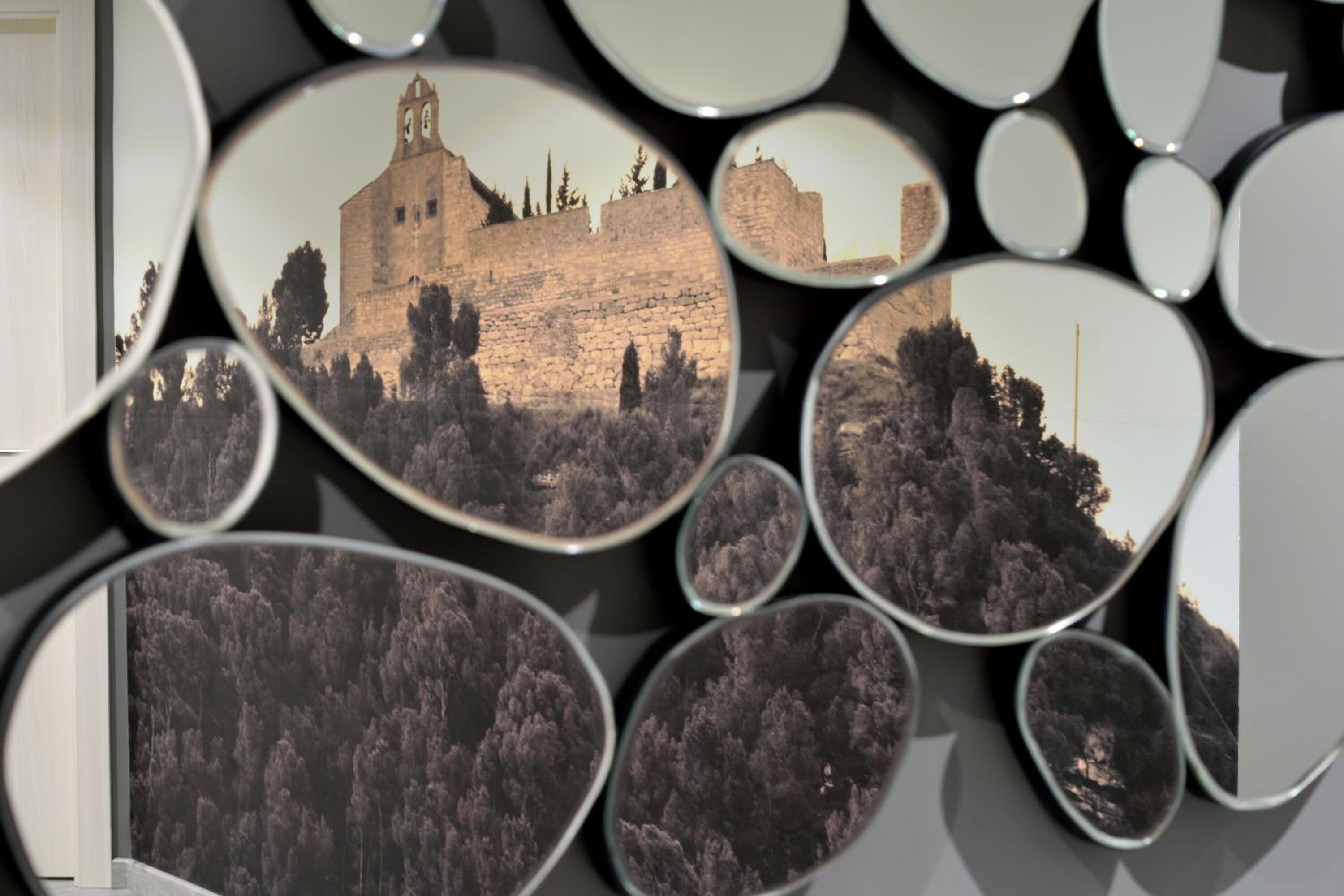 A wall of mirrors reflecting a castle-like structure with a tower, surrounded by trees.