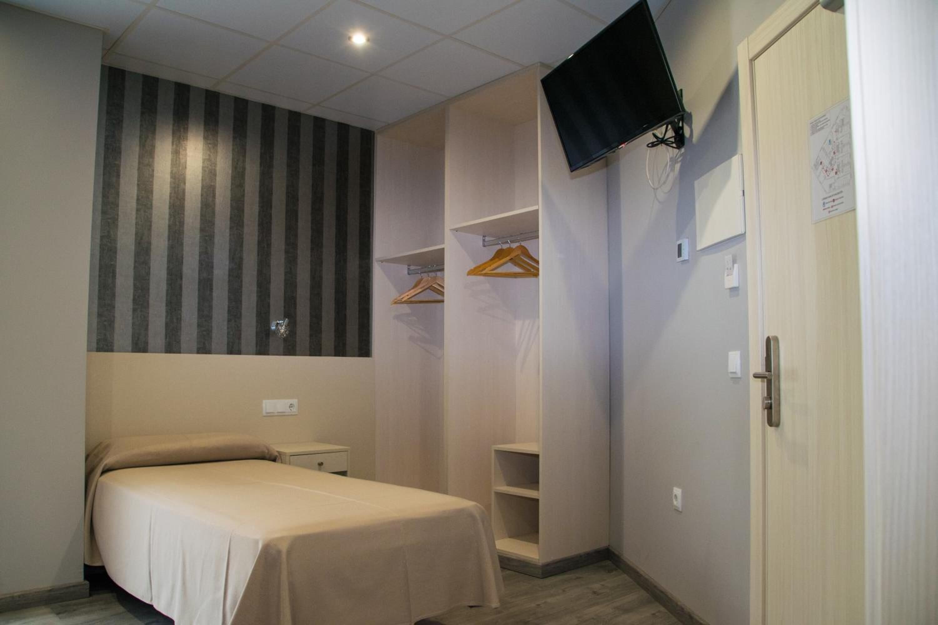 Quarto com cama, guarda-roupa, televisão fixada na parede e porta com puxador.