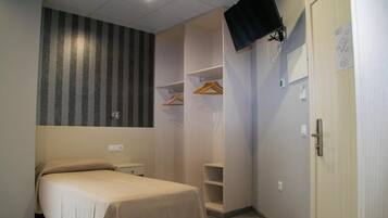 Quarto com cama, guarda-roupa, televisão fixada na parede e porta com puxador.