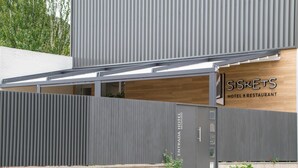 Een moderne hotelentree met een grijze gevel, een houten receptiebalie en een bord met de tekst 'SISKETS HOTEL RESTAURANT'.