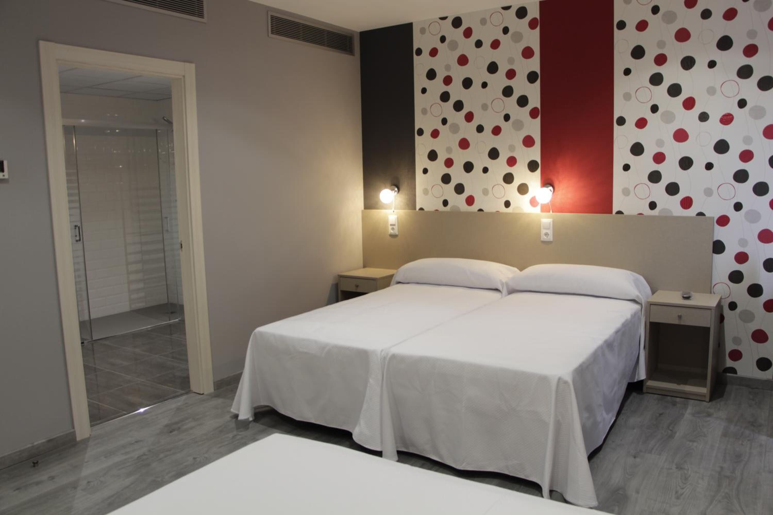 A double bed with white bedding, two bedside tables, and a wall with a polka dot pattern.