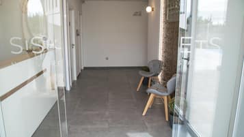 A hotel reception area with a glass wall, two grey chairs, a wooden bench, and a small potted plant.