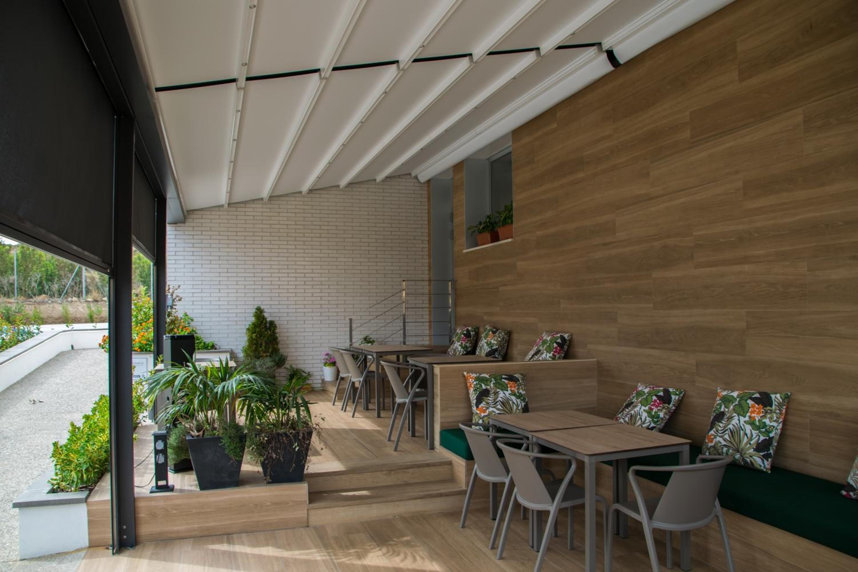 An indoor seating area with wooden tables and chairs, potted plants, and a staircase leading to an upper level.