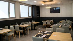 Een modern restaurant met meerdere tafels en stoelen, grote ramen en een flatscreen televisie aan de muur.
