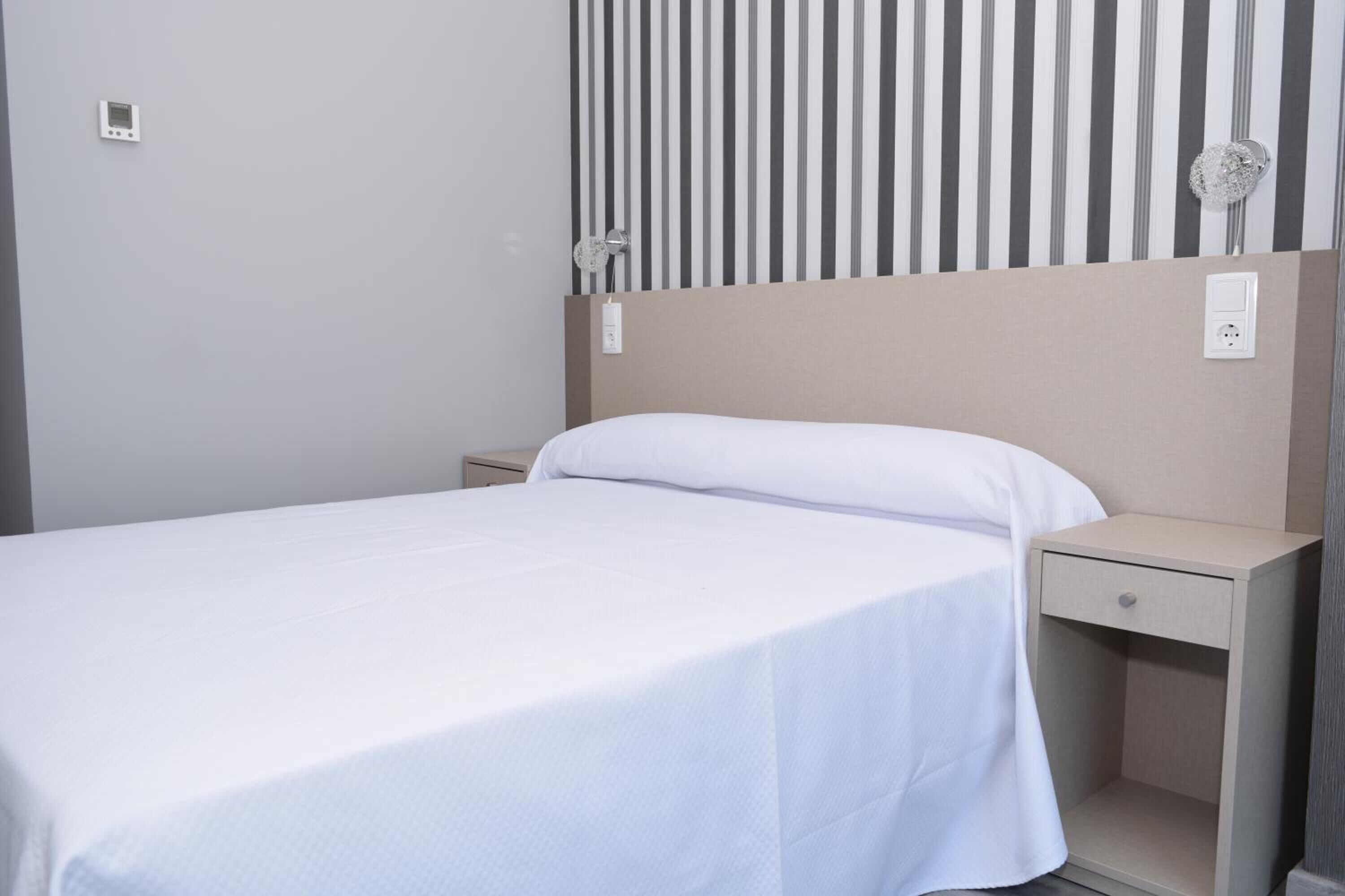 A single bed with a white bedspread, a nightstand with a drawer, and a wall-mounted light fixture.