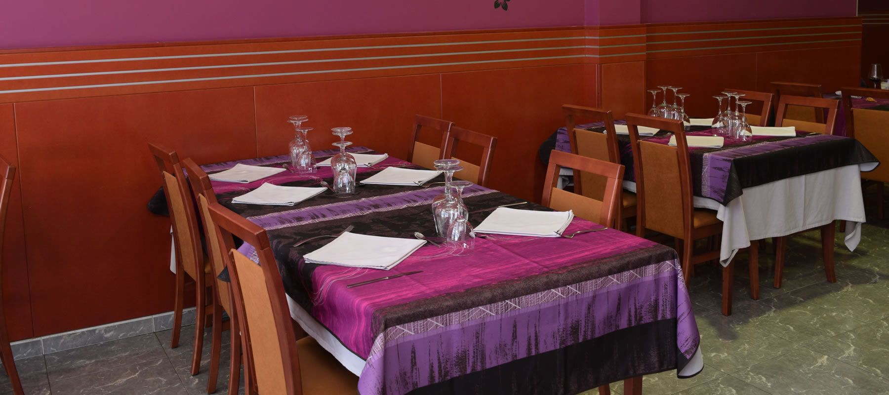 A dining area with tables set for multiple guests, each with a white tablecloth, wine glasses, and cutlery.