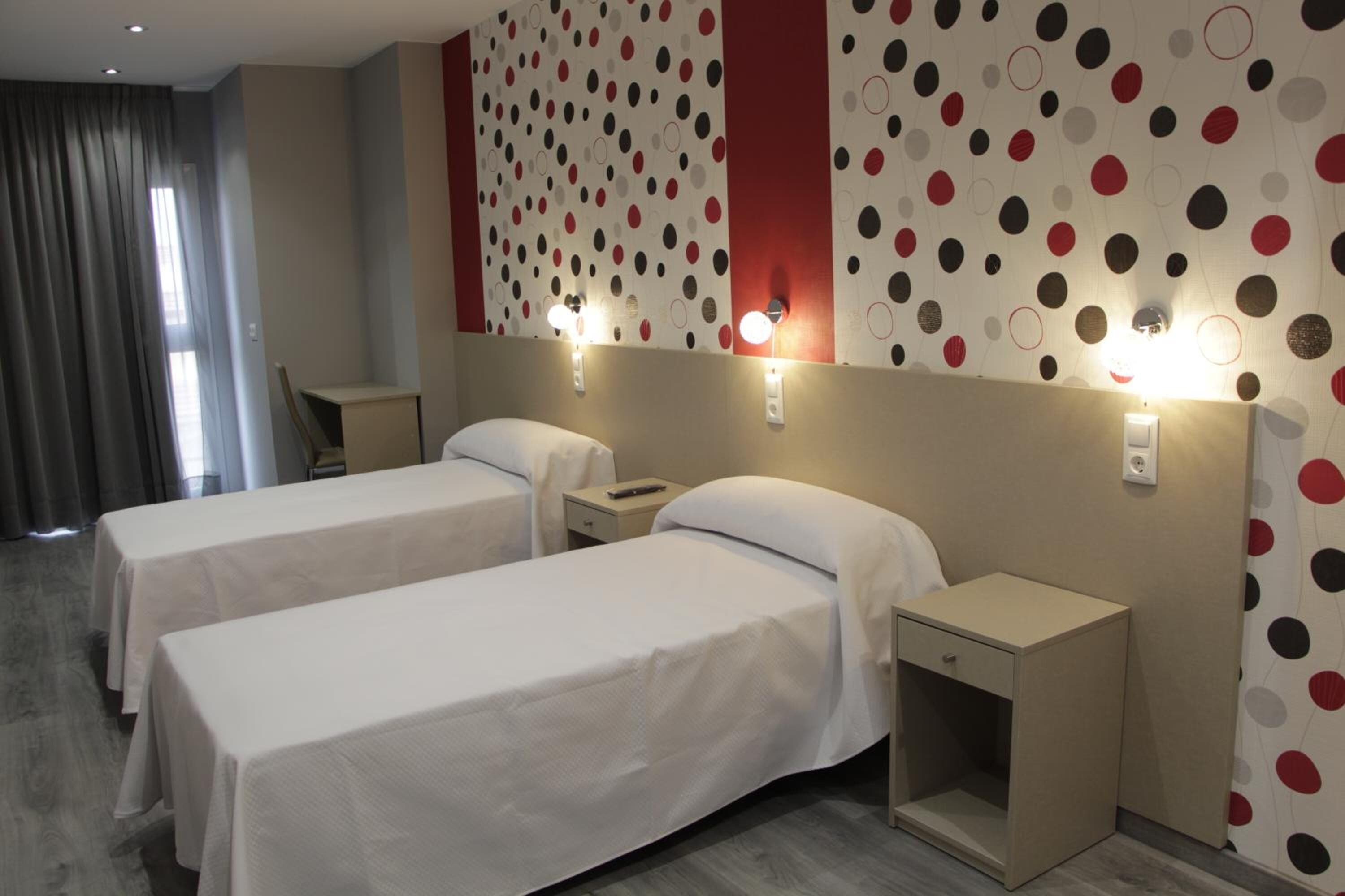 A hotel room with two beds, a bedside table, a nightstand, and a wall with a polka dot pattern.