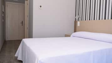 A hotel room with a single bed, a wooden door, a small bedside table, and a striped wallpaper on the wall.