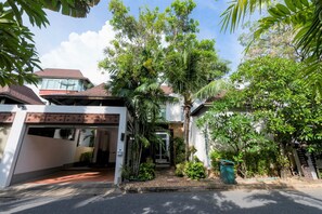 A residential property with a covered driveway, a garage, and a well-maintained garden with various plants and trees. - Tropical Garden Paradise Villa (Sattahip)