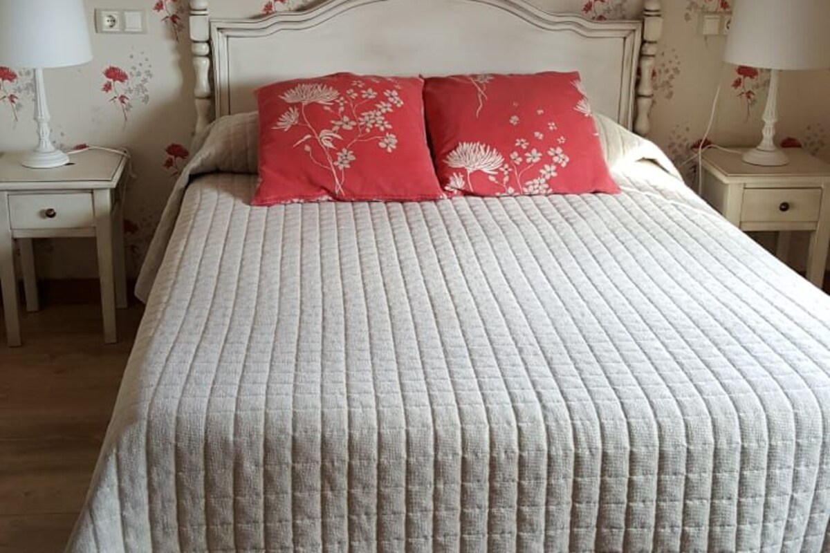 A bed with a headboard, two bedside tables, and a floral wallpaper pattern.