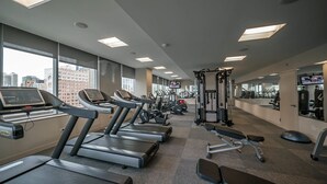 Een fitnessruimte met loopbanden, krachttoestellen en een televisiescherm.
