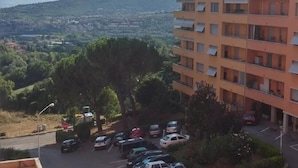 Un edificio residencial de varios pisos con balcones, un estacionamiento con varios coches y una vista de un paisaje montañoso al fondo.