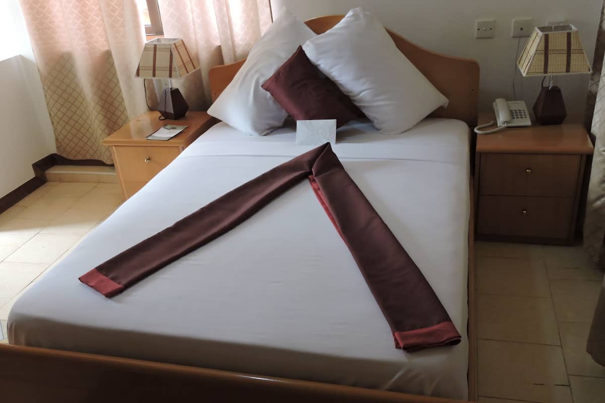 A neatly made bed with white and brown linens, a bedside table with a lamp, a phone, and a nightstand with a lamp.