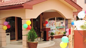 A hotel entrance with a tiled roof, a large potted plant, and colorful balloons.