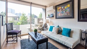 Una sala de estar moderna con un sofá, un sillón, una mesa de centro y un ventanal con vistas a la ciudad.