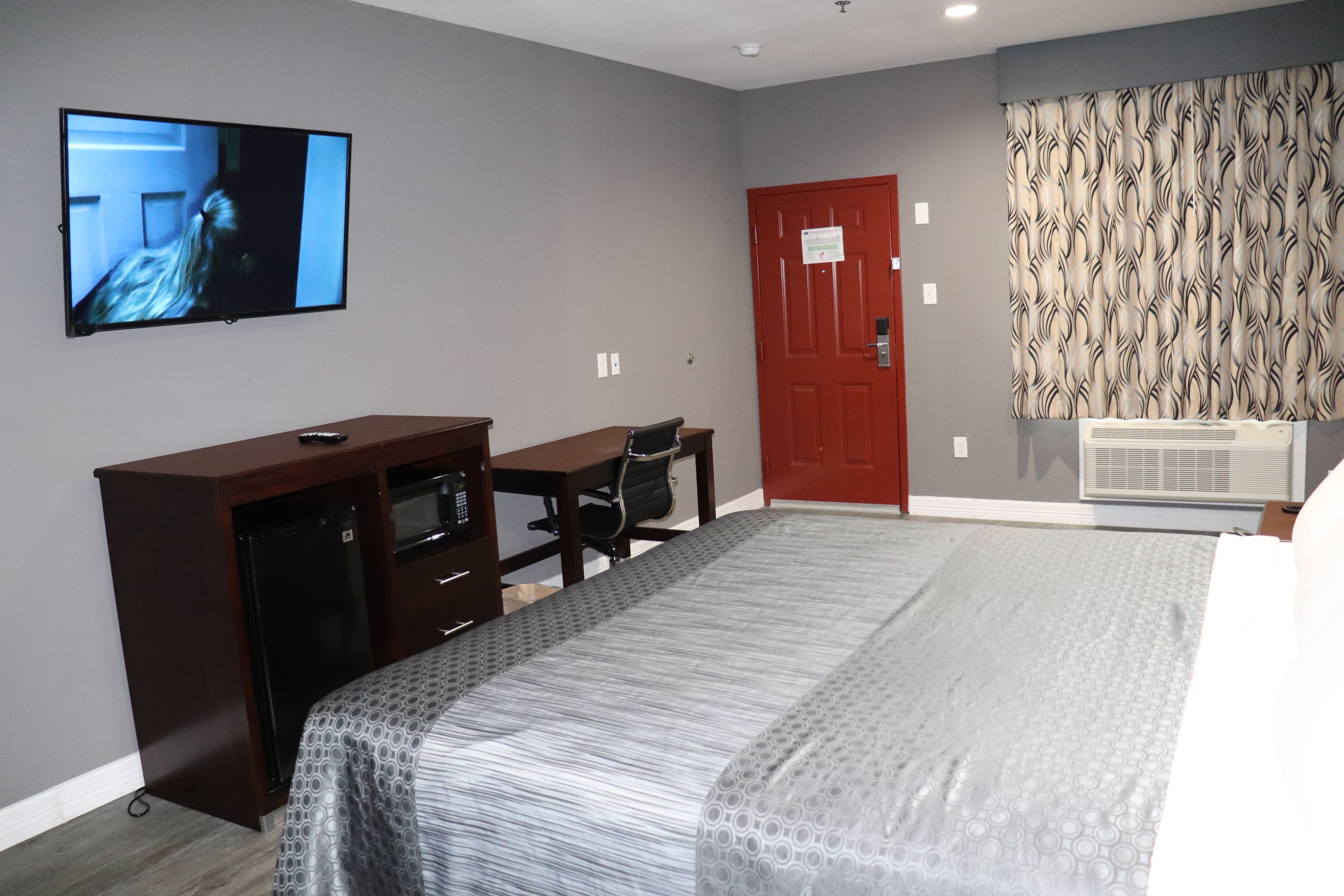 Une chambre d’hôtel avec un lit, un bureau, une télévision, une armoire et une porte rouge.