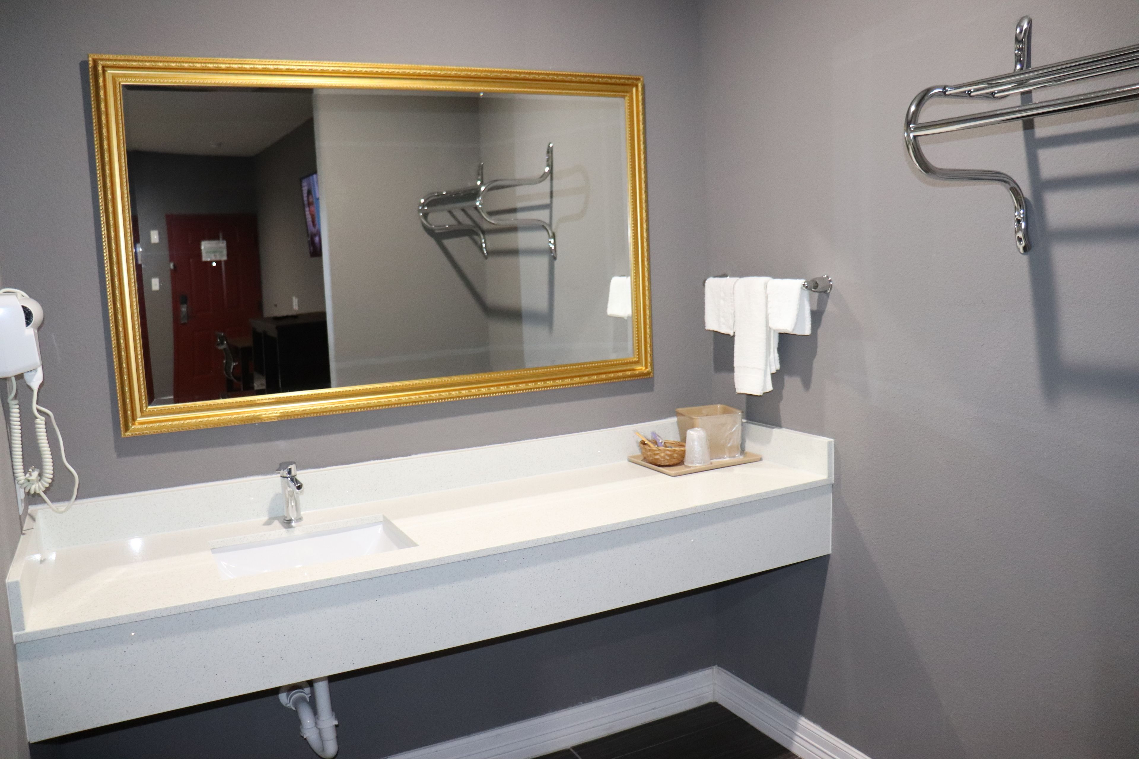 A bathroom with a white sink, a large mirror with a gold frame, a towel rack, and a shower head.
