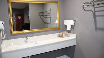 A bathroom with a white sink, a large mirror with a gold frame, a towel rack, and a shower head.
