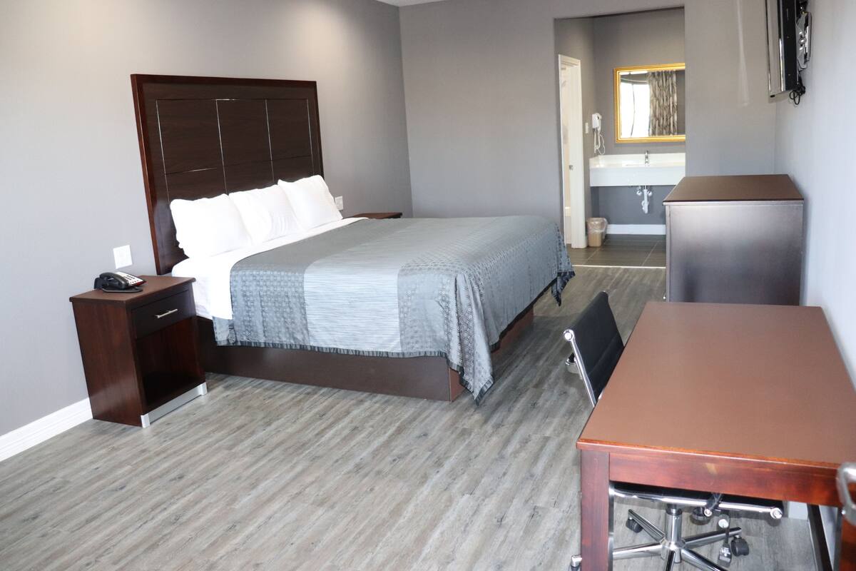 A hotel room with a bed, bedside table, desk, and a bathroom visible through an open door.