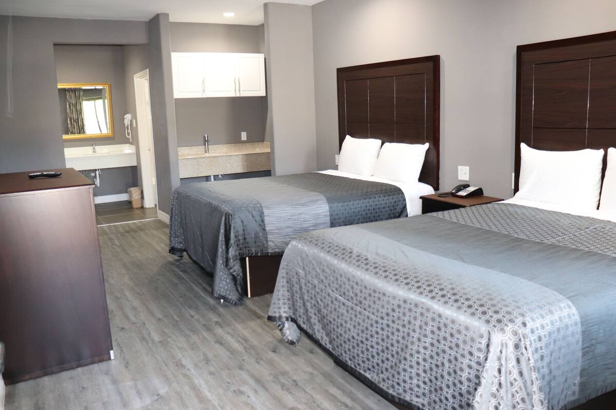 A hotel room with two beds, a wooden desk, a mirror, and a bathroom with a sink and mirror.