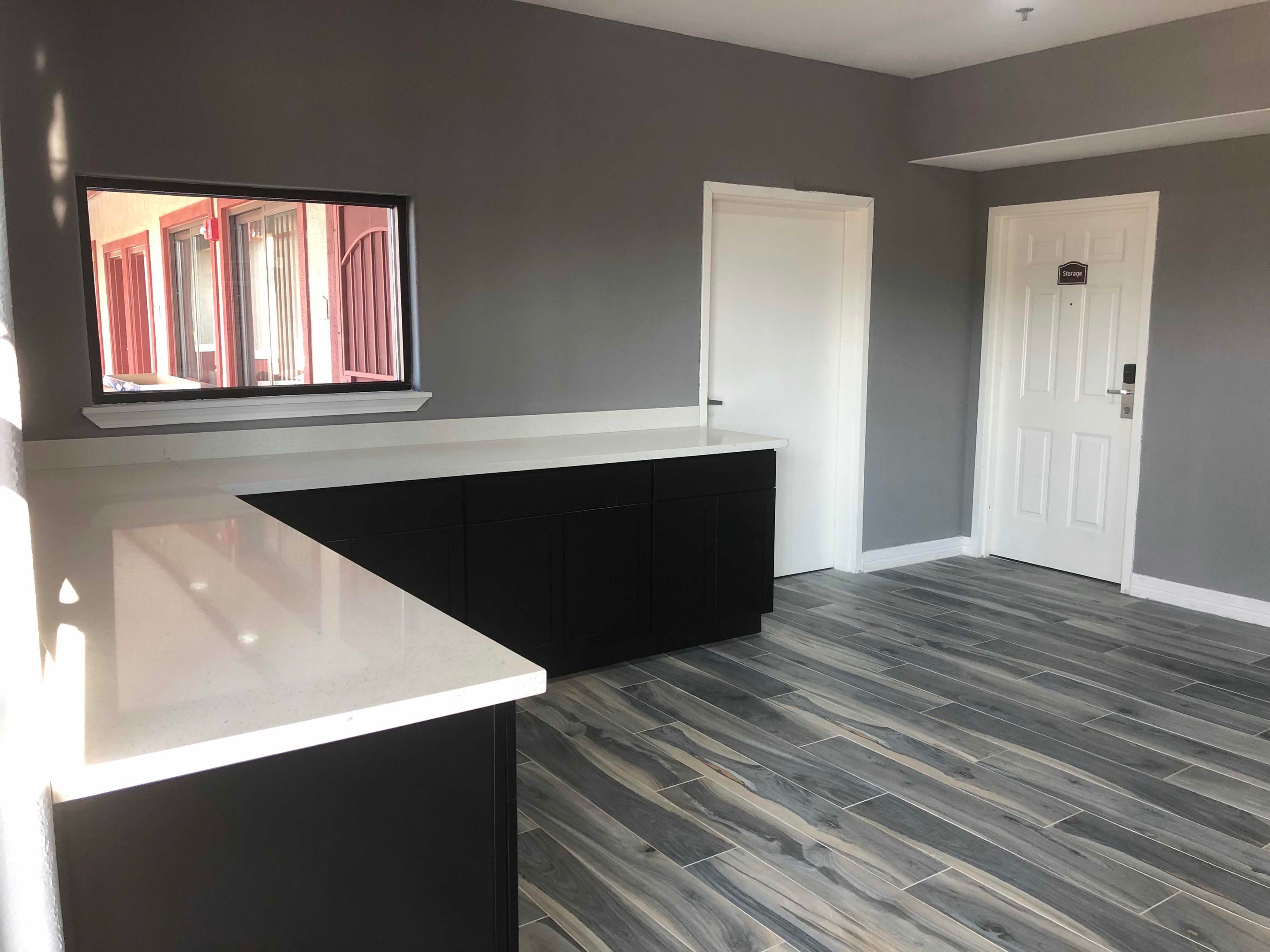 A modern kitchen with a white countertop, dark cabinets, and a window with a view of a building.