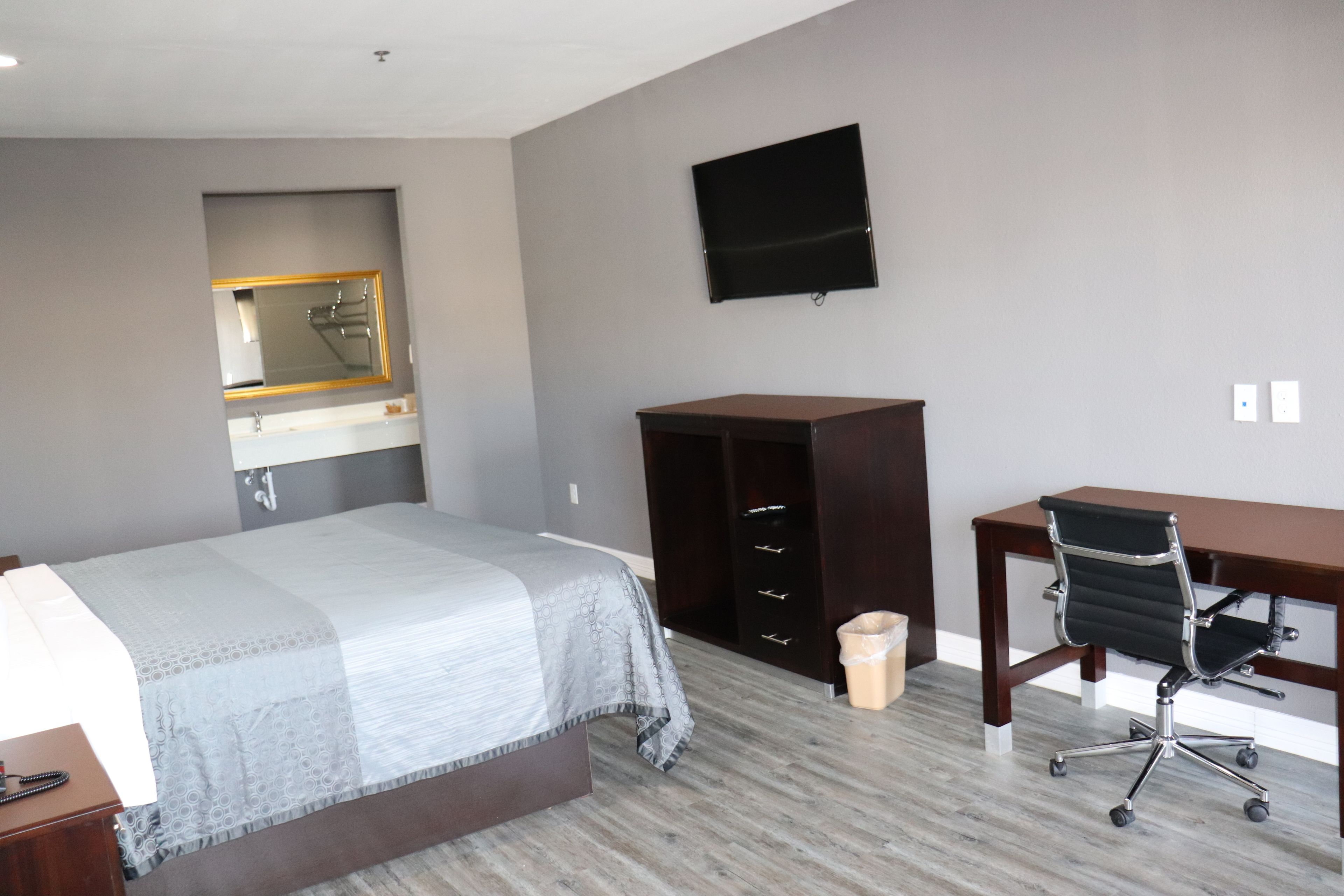 A hotel room with a bed, a desk, a chair, a TV, a wardrobe, and a mirror.