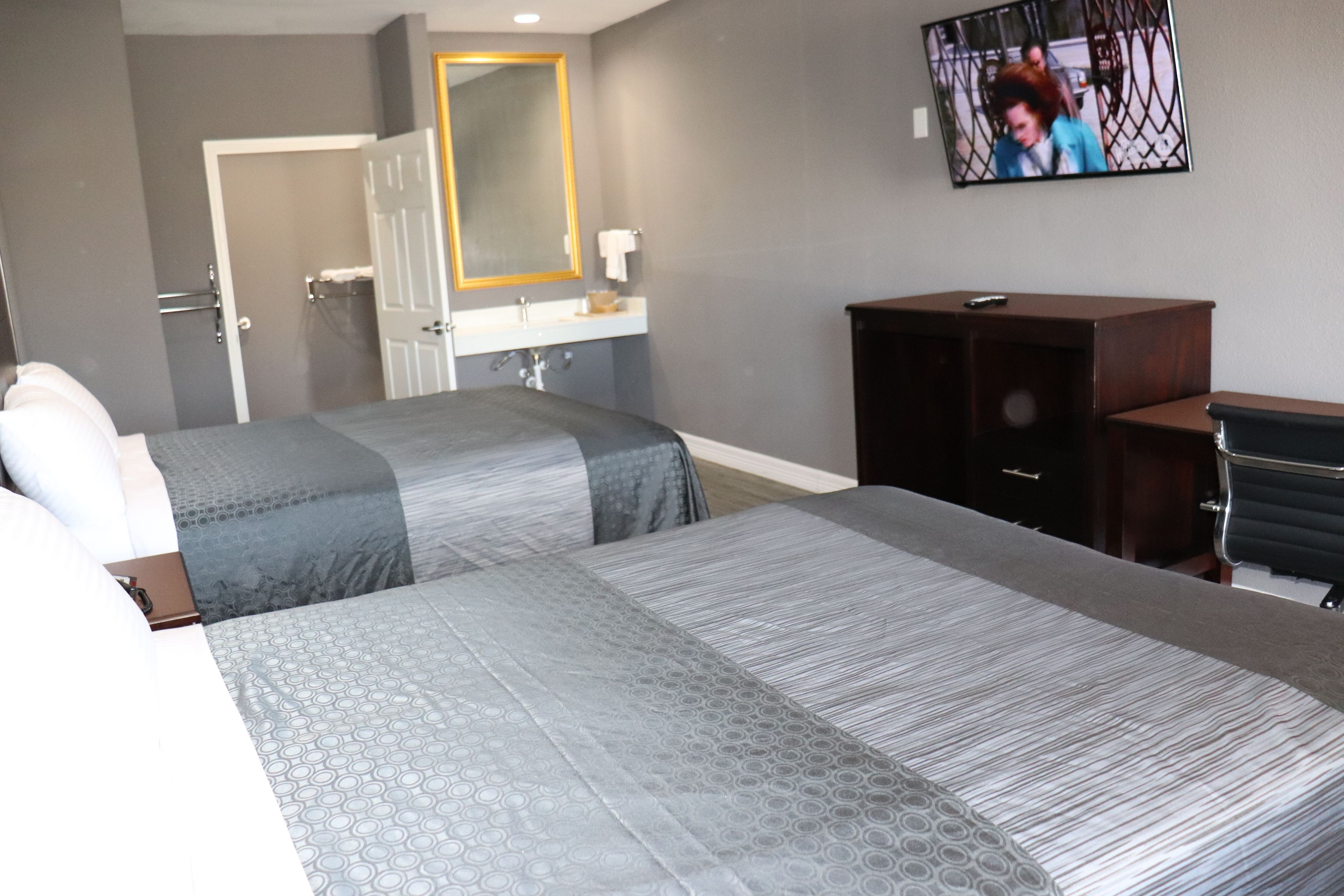 A hotel room with two beds, a bathroom, a TV, and a desk.