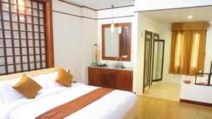 Habitación de hotel con una cama grande, un aparador de madera, un espejo y un baño visible a través de una puerta abierta.
