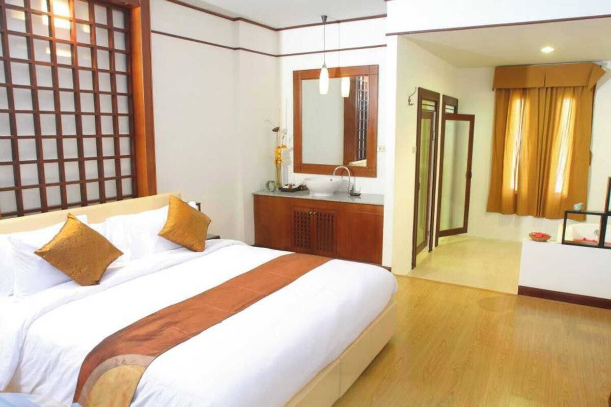 A hotel room with a large bed, a wooden dresser, a mirror, and a bathroom visible through an open door.