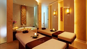 Een spa-ruimte met twee massagetafels, een badkuip en wandlampen.
