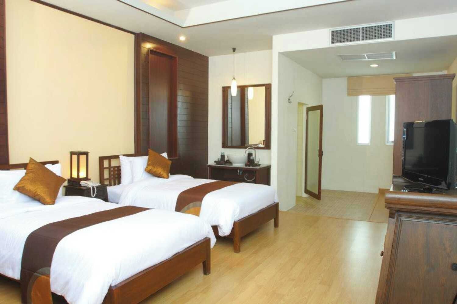 A hotel room with two beds, a TV, a desk, and a mirror.