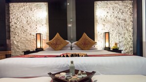 Een hotelkamer met een groot bed, twee nachtkastjes, een dienblad met snacks en decoratieve kussens.