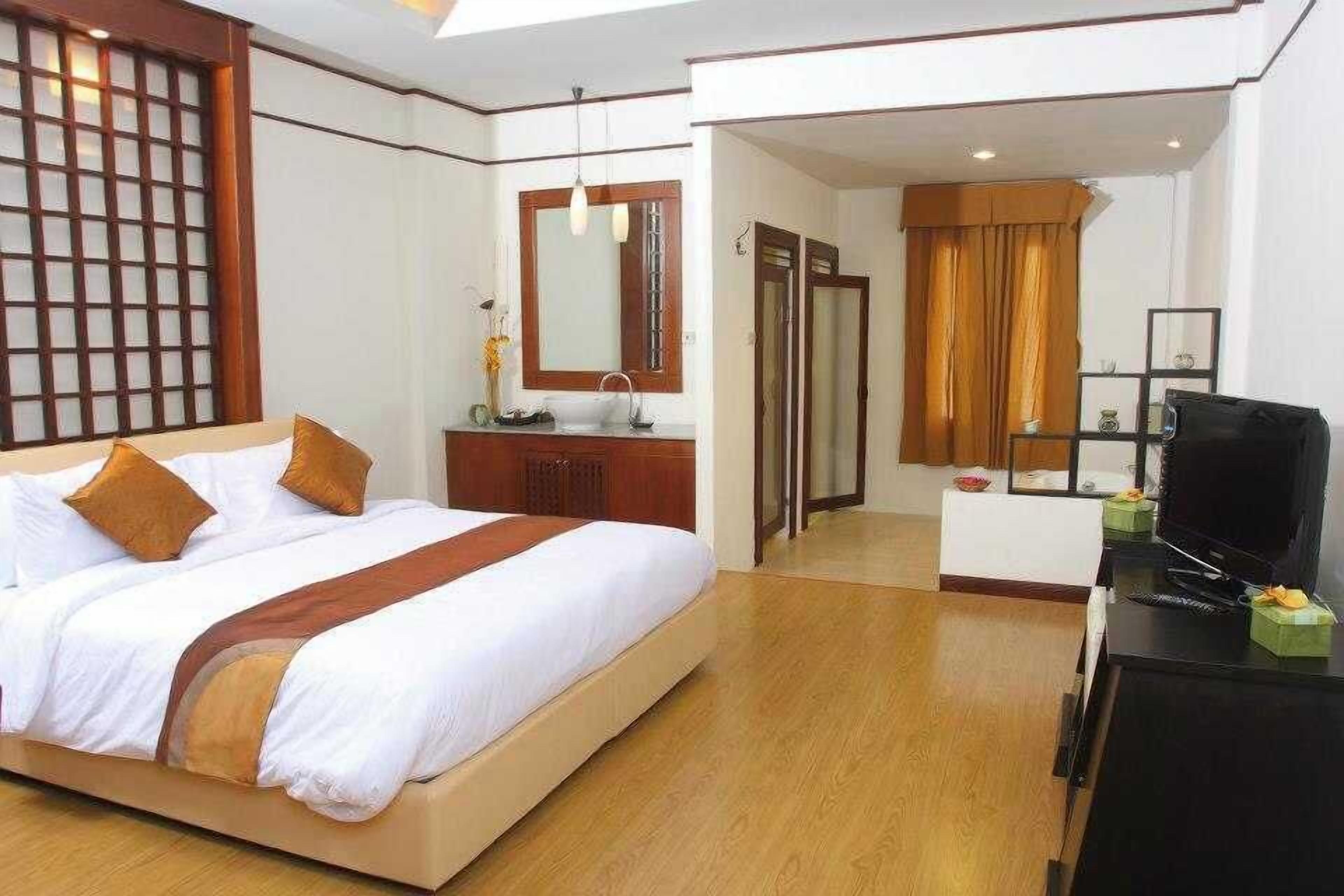 Una habitación de hotel con cama, mesita de noche, televisión y baño visible a través de una puerta abierta.