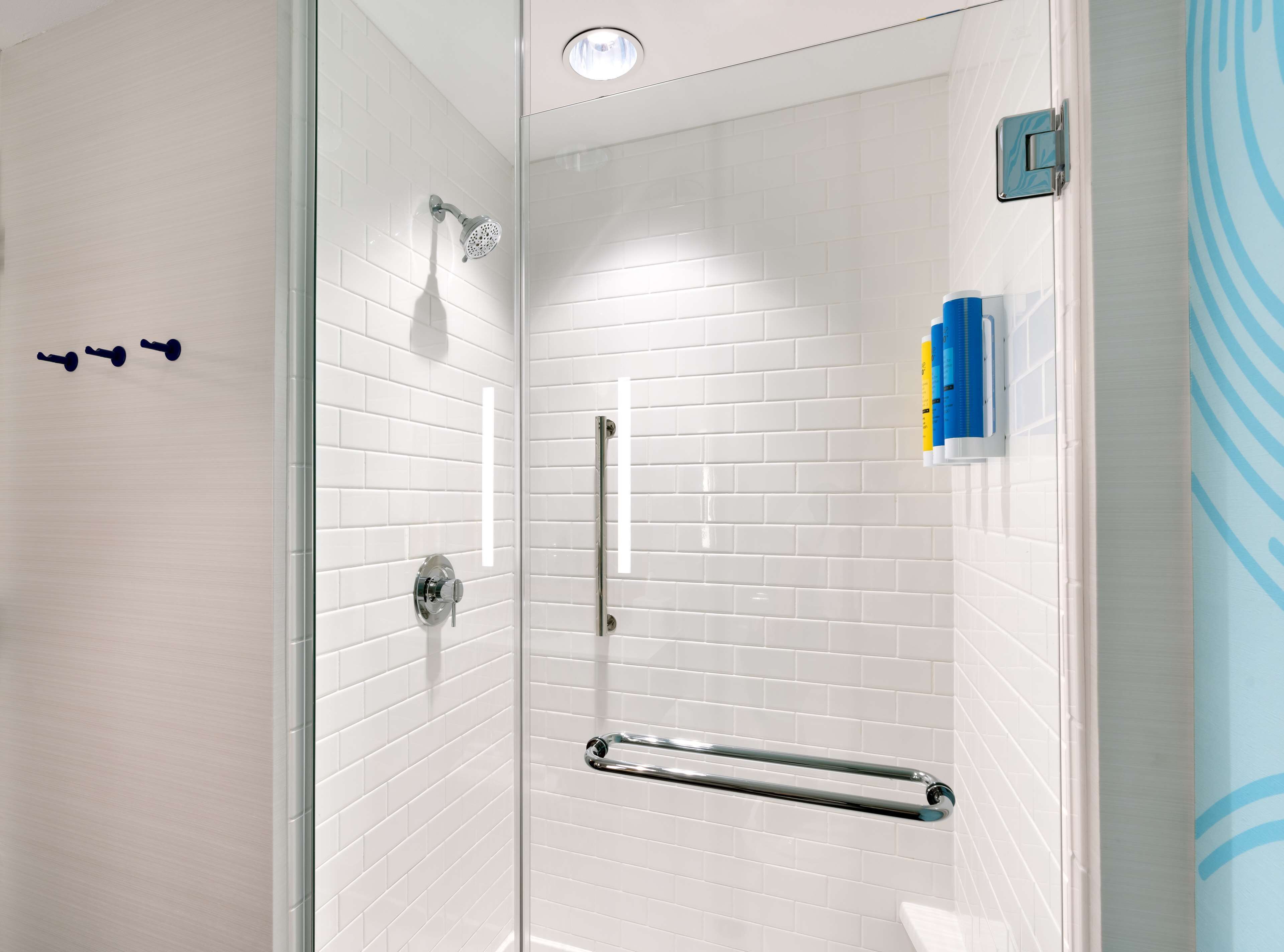 A modern shower with white tiled walls, a glass door, and a handrail.
