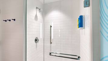 A modern shower with white tiled walls, a glass door, and a handrail.