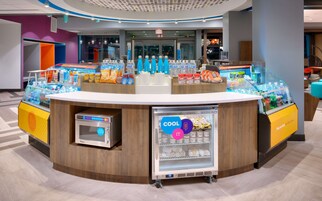 Una estación autoservicio de bebidas y aperitivos, con un refrigerador y una máquina de café.