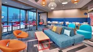 A modern lounge area with seating, tables, and a view through large windows. - Tru By Hilton St George, UT (St. George)