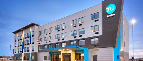 A modern hotel with a prominent 'tru by Hilton' sign, multiple floors, and a well-lit entrance.