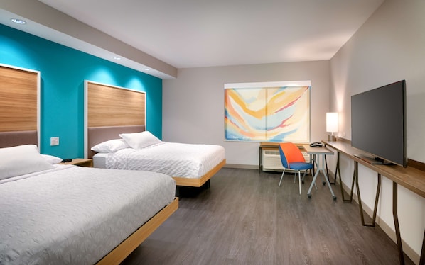 A hotel room with two beds, a desk with a chair, a TV, and a large abstract painting on the wall.
