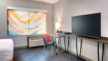 Habitación de hotel con cama, escritorio con televisor de pantalla plana, silla, calefactor y un cuadro abstracto grande en la pared.