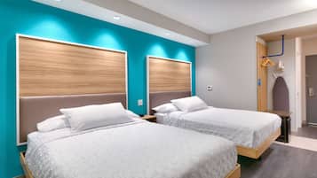 A hotel room with two beds, wooden headboards, teal walls, and a small table with a chair.