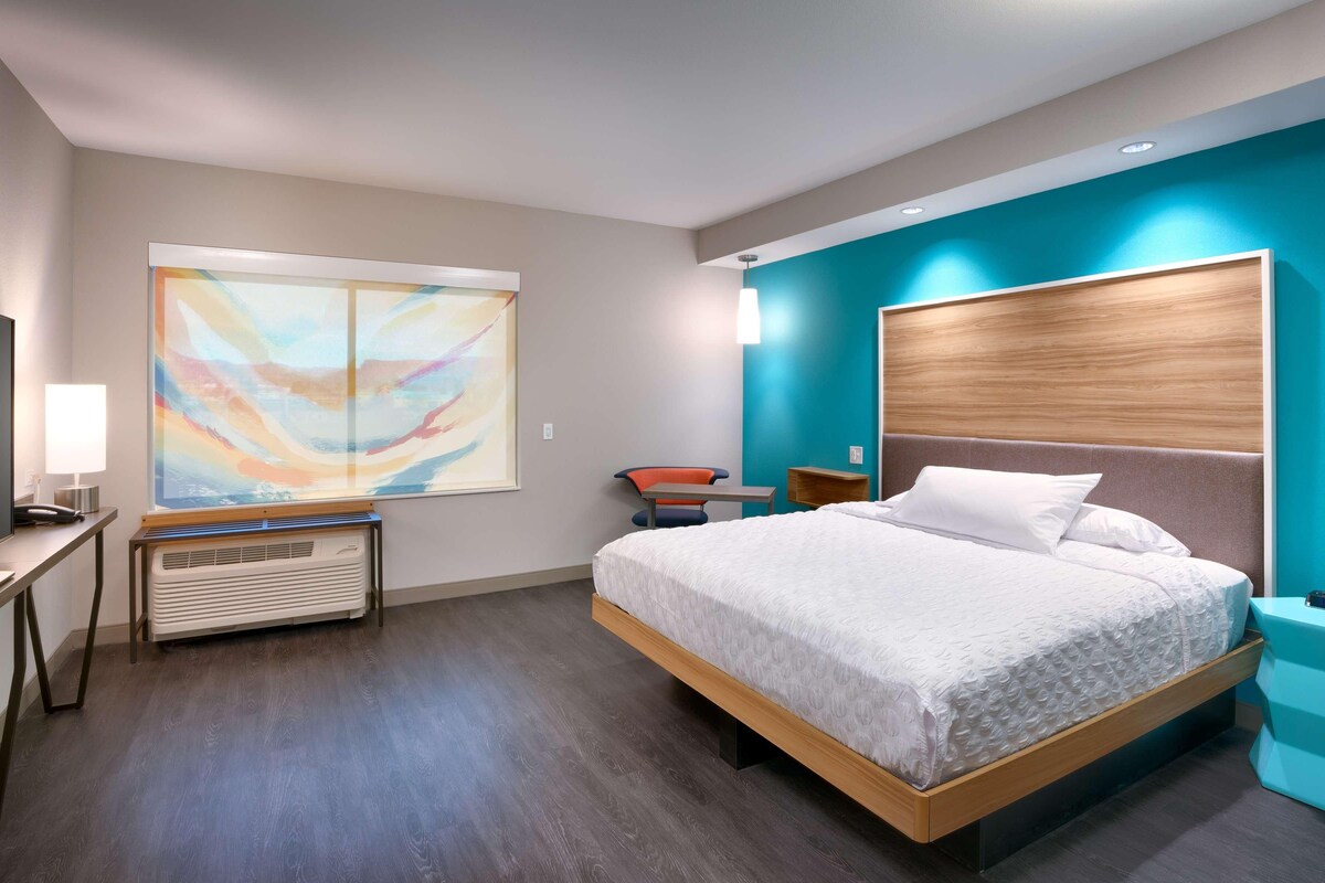 A modern hotel room with a large bed, a desk, a chair, and a TV.