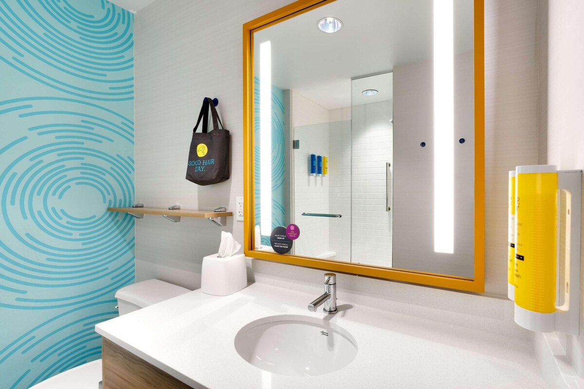A modern bathroom with a white sink, a large mirror, and a towel dispenser.