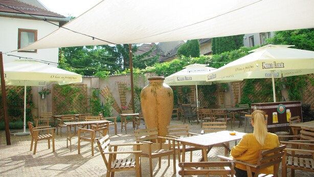 An outdoor patio with wooden tables and chairs, large umbrellas, and a prominent vase. - B13 Hostel (Sibiu)