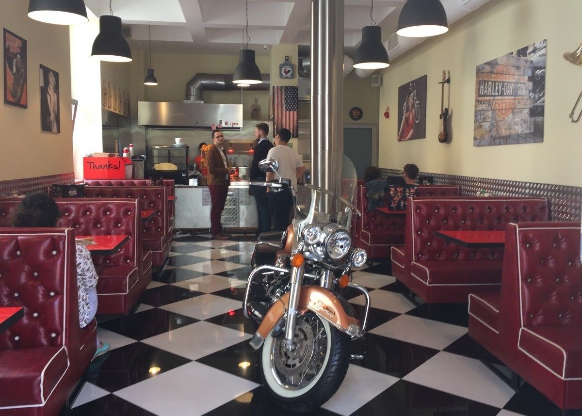 Un restaurante con asientos tapizados en rojo, una motocicleta en el centro y piso de baldosas a cuadros.