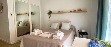 A bedroom with a bed, a wardrobe, a bedside table, a plant, and a window with curtains.